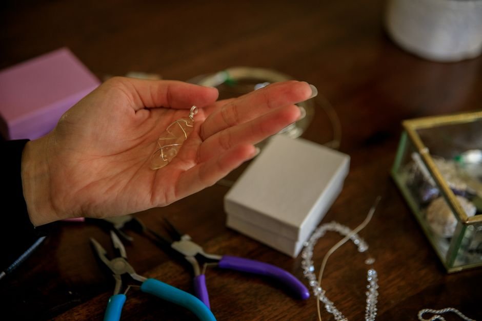 Broken Crystal Jewelry Ideas — Wire-Wrapping a Fragment Into a Pendant Hand holding a wire-wrapped crystal pendant at a jewelry bench with pliers, repurposing a broken stone