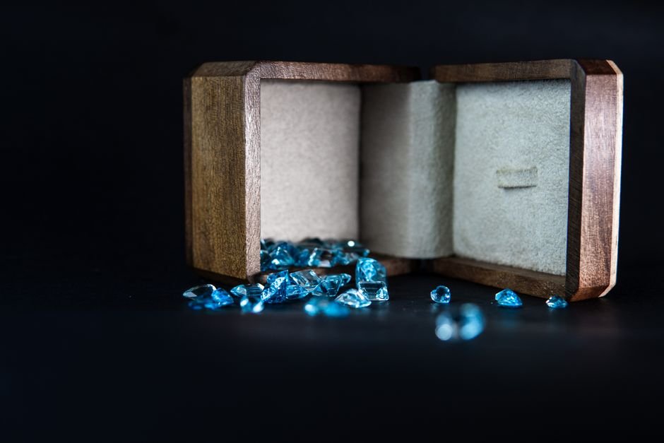 Dyed Glass Crystals — Why Fakes Are So Cheap and Easy to Produce Sparkly blue glass gems spilling from a wooden box, the cheap colored glass often sold as natural crystal