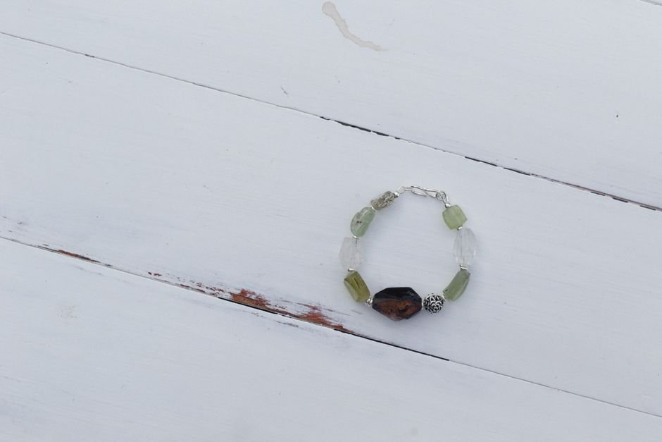 why did my crystal bracelet snap — gemstone bead bracelet lying on a white wooden table