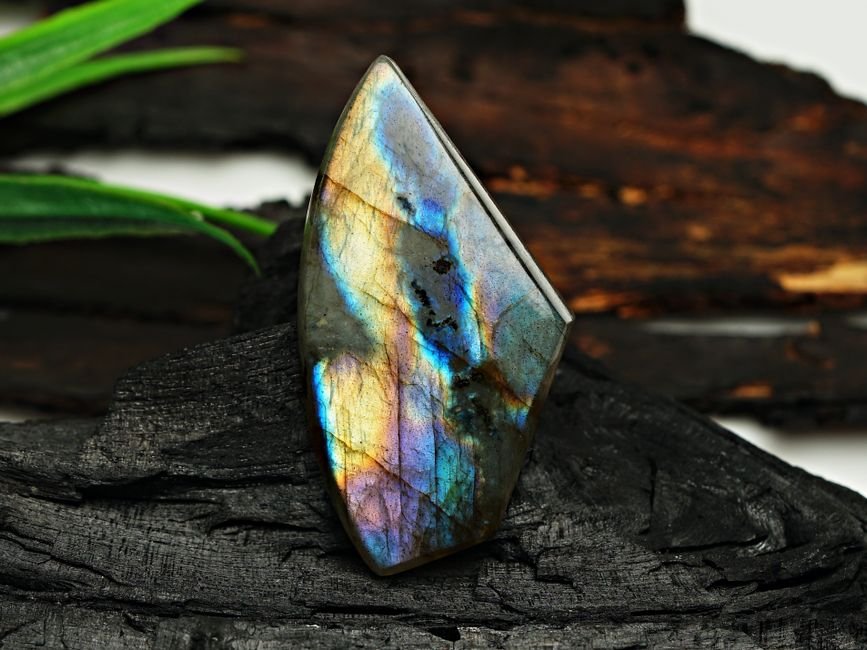 Iridescent labradorite stone on dark wood, a crystal traditionally described as needing a slow attunement period