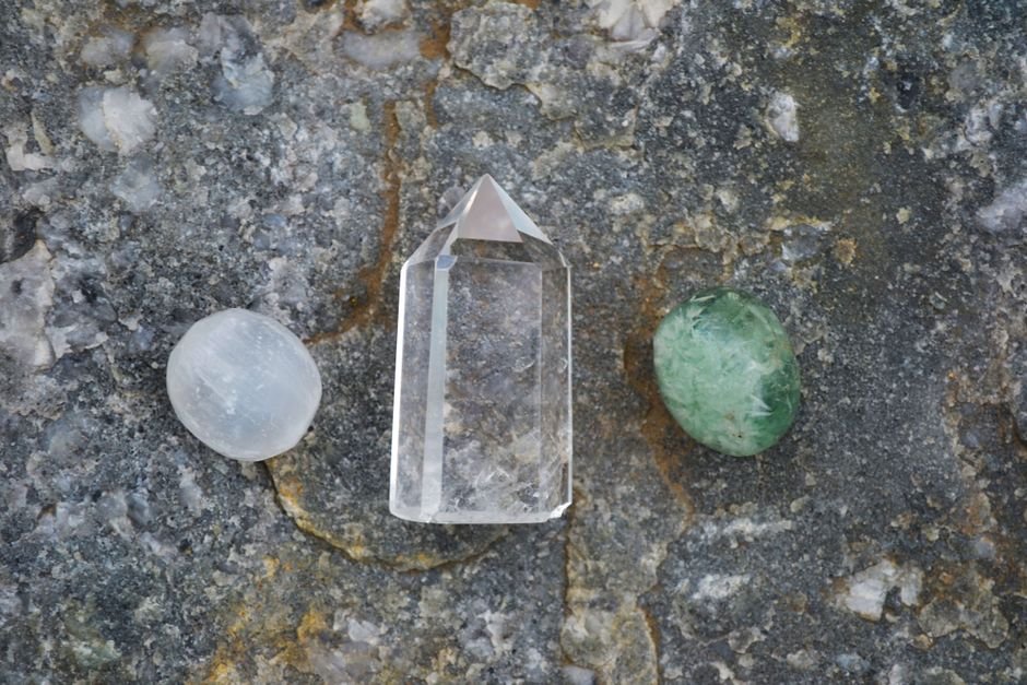 Clear quartz point and tumbled stones lying on natural rock, inert minerals that sit in soil unchanged for years