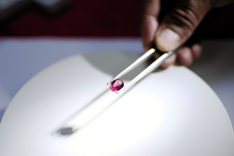 Lapidary Re-Cutting a Gemstone — Removing Damage Instead of Gluing It Hand holding a red gemstone with tweezers under a lamp, assessing it for lapidary re-cutting