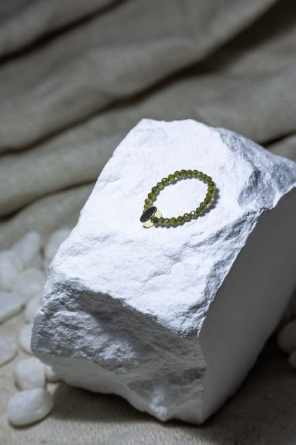 Moldavite-Inspired vs Fake — Disclosure Is the Difference Green beaded bracelet displayed on white stone, the kind of honestly labeled moldavite-style glass jewelry that isn't a fake
