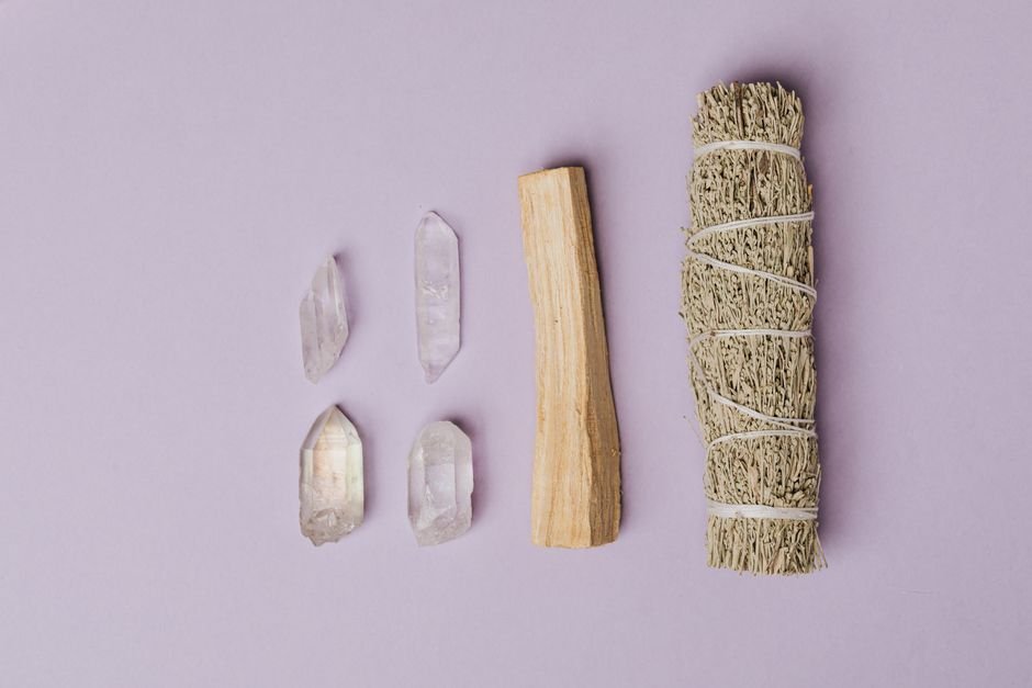 Clear quartz crystals arranged beside a sage smudge stick and palo santo wood used to cleanse crystals in spiritual practice