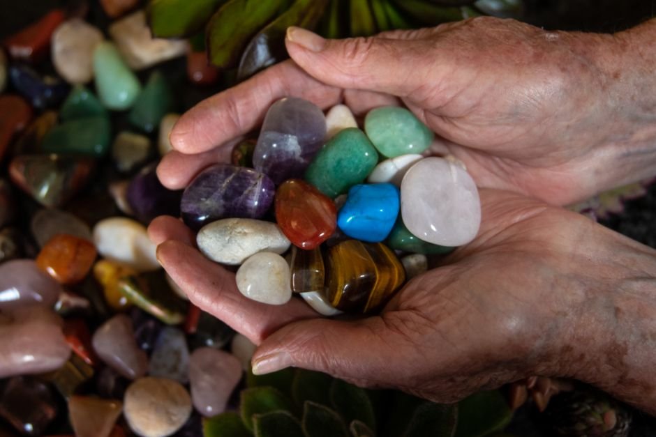 Elderly hands cradling a collection of well-loved tumbled crystals gathered over many years of use