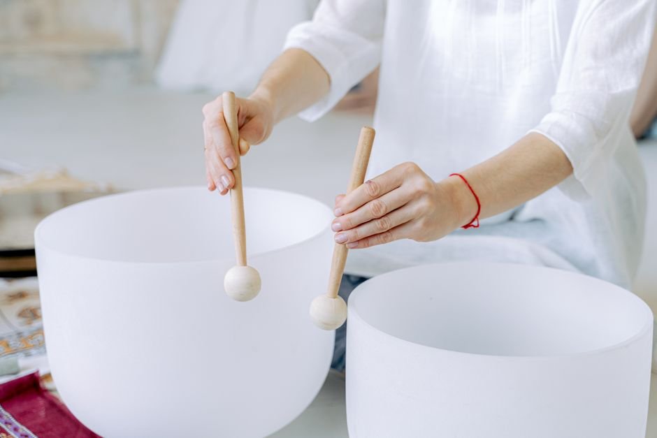 How to Recharge Crystals Safely — Sound Bath Instead of Direct Sunlight Woman playing white crystal singing bowls with mallets, a light-safe sound bath method for recharging crystals