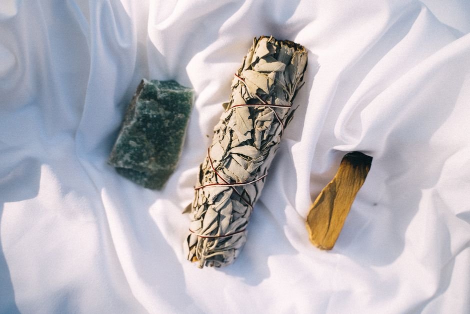 Sage smudge stick, palo santo, and green aventurine laid out on white fabric for a crystal cleansing and intention reset