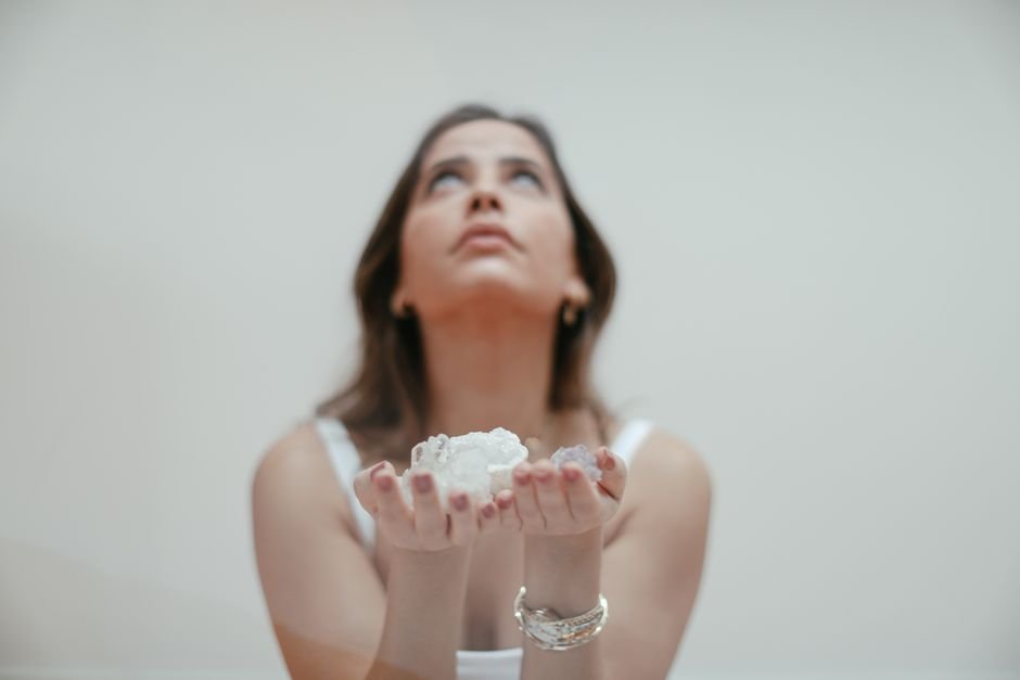 Woman holding clear crystals in cupped hands with an expectant upward gaze, showing how attention and expectation drive felt effects