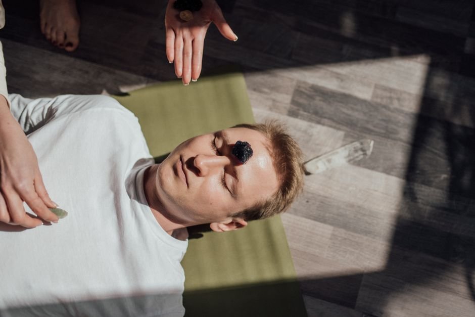 Practitioner's hands hovering over a man receiving a crystal healing session with a stone on his forehead