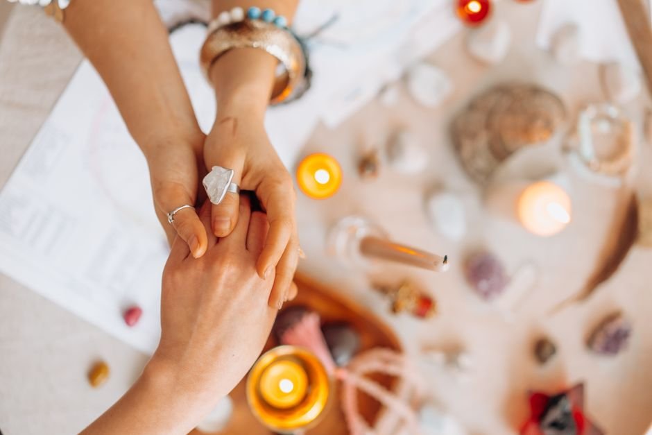 Recharge a Crystal Step by Step — Cleanse, Rest, and Reset the Intention Hands holding a raw crystal ring over a candle-lit ritual table while resetting a fresh intention for the stone