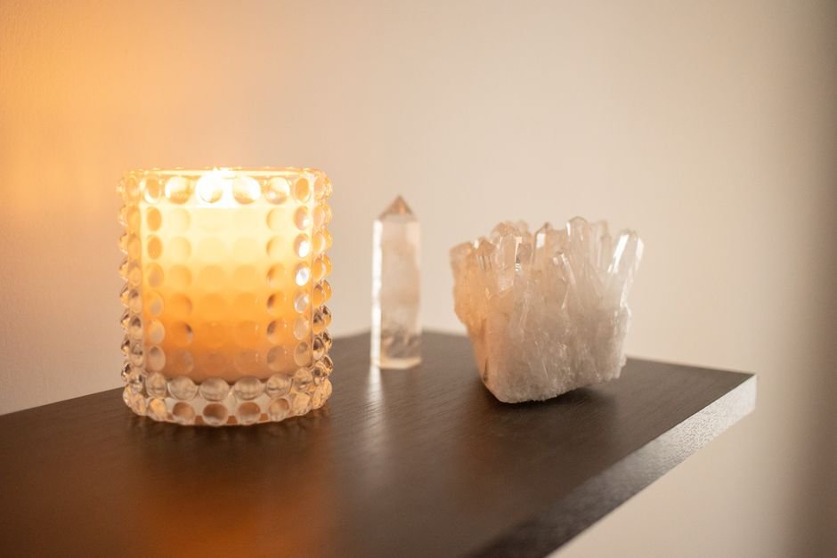 How to Fix a Blocked Crystal — Move Your Stones to an Intentional Space Clear quartz tower and crystal cluster displayed on a tidy dark-wood shelf beside a lit candle in an intentional space
