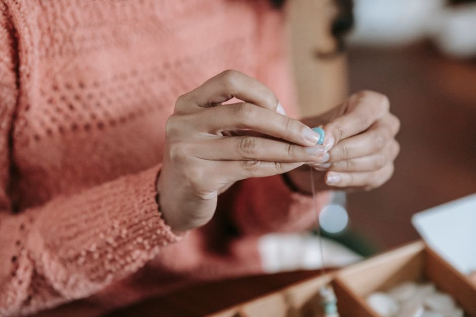 Hands restringing beads onto fresh elastic cord at a craft table
