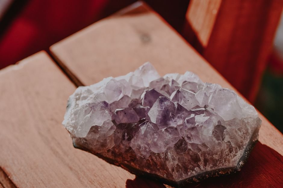 pale faded amethyst cluster sitting in direct sunlight on a wooden chair, showing can crystals lose their power through sun fading