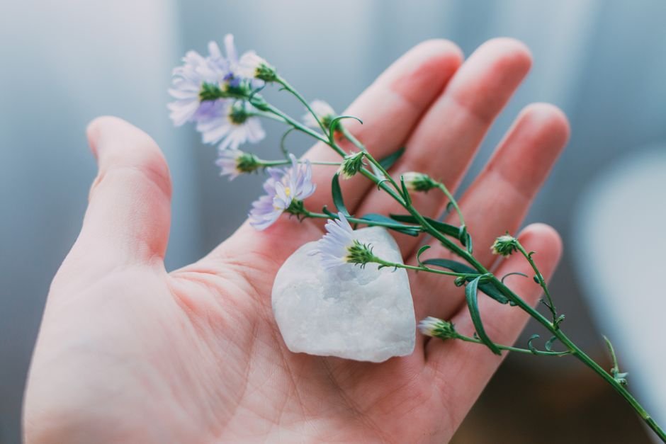 Crystal Feels Warm or Tingly — Body Heat, Touch and Suggestion Explained Clear quartz crystal resting in an open palm with wildflowers, showing the warmth and touch sensations people report as activation