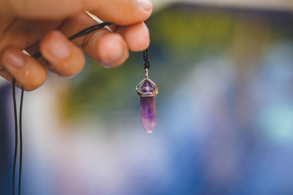 Hand holding a purple amethyst pendant up against the light to check for the round static bubbles that reveal glass