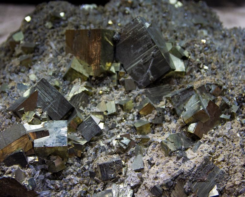 Close-up of golden pyrite crystals showing their geometric cubic faces, a stone unbothered by sunlight but degraded by humid air